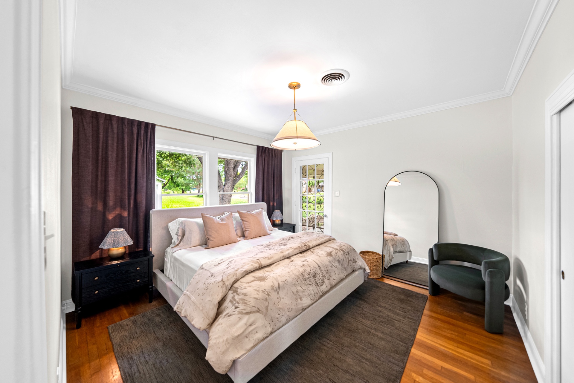 Primary bedroom with upholstered king bed, plum linen drapes, and arched mirror at Casa Thorman