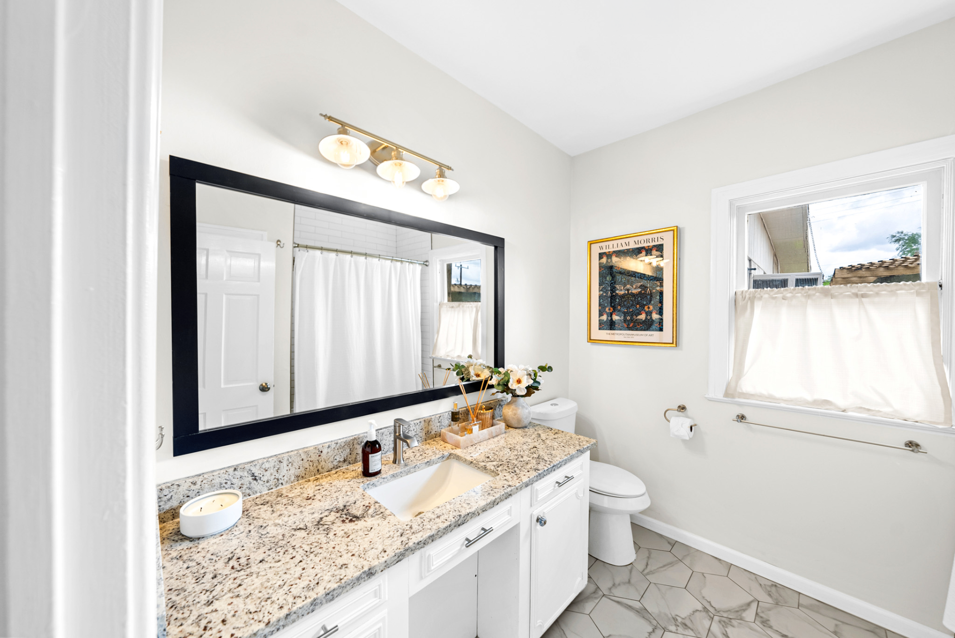Renovated primary bathroom with framed mirror, granite vanity, and marble floor at Casa Thorman
