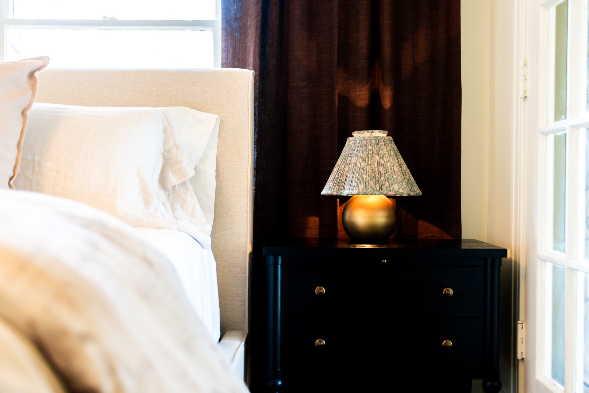 Black nightstand with brass lamp and dark linen curtains at Casa Thorman